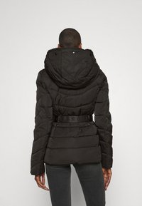 Sort pufferjakke med hætte og bælte i taljen, med quiltet struktur og fremtrædende logo på bæltet. Standard pasform, lange ærmer.
