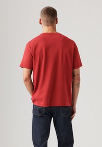 Rød bomulds T-shirt med korte ærmer og en lige kant, parret med mørke denim jeans med klassiske baglommer og gul syning.