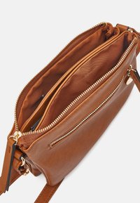 Brun læder crossbody taske med flere lynlåslommer og justerbar rem på en hvid baggrund.