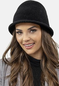 Chapeau seau noir texturé avec une couronne ronde et un large bord, porté en gros plan dans un cadre portrait contre un fond clair.