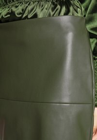Falda de imitation piel verde oliva con una textura suave, que presenta un diseño sin costuras y una cinturilla elástica en una tela a juego en la parte superior.