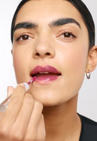Produit à lèvres appliqué sur les lèvres, couleur baies riche, finition brillante, avec un applicateur fin. La peau a une texture lisse et naturelle.