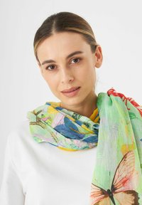 Écharpe en soie multicolore avec des motifs floraux et de papillons sur un fond vert clair, drapée autour du cou.