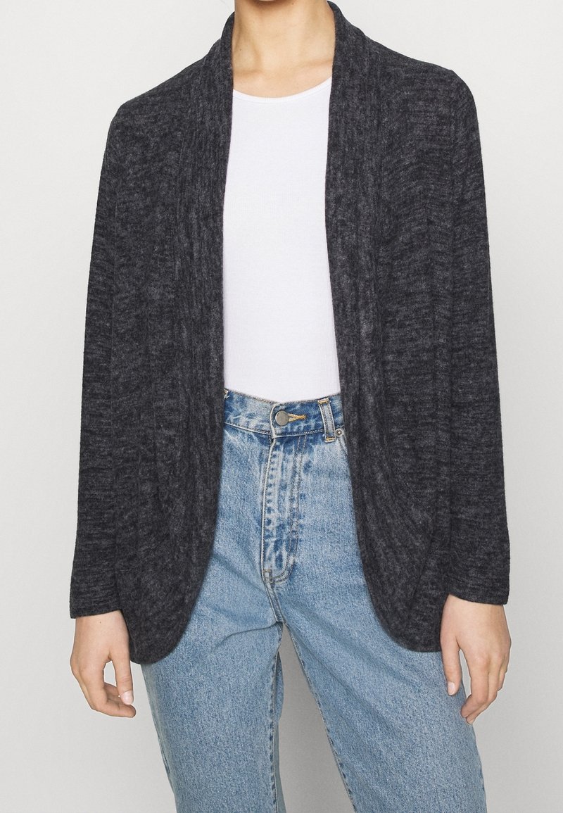 Cardigan lavorato a maglia grigio scuro con apertura sul davanti, maniche lunghe e finitura testurizzata. Indossato sopra un top bianco e jeans a vita alta blu chiaro.