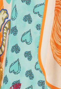Bunt gemusteter Stoff mit einem türkisfarbenen Grund und schwarzen Leopardenherz-Drucken, umrandet von orangefarbenen Akzenten sowie komplexen blumen- und tierähnlichen Designs.