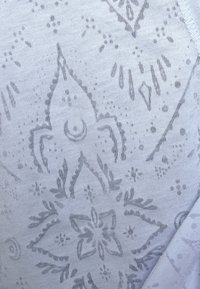 Tessuto azzurro chiaro con un sottile motivo floreale di tonalità più scura, caratterizzato da disegni intricati e una superficie liscia. Alcune cuciture visibili.