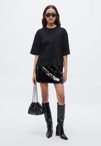 Czarny oversize t-shirt, czarno-srebrna mini spódnica z cekinami, błyszczące czarne kozaki za kolano oraz mała czarna torebka na ściągacz.