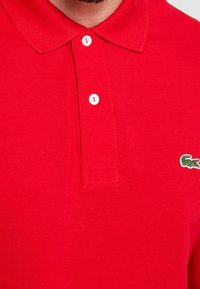 Polo shirt rossa realizzata in tessuto testurizzato, con colletto a tre bottoni e logo verde ricamato sul petto.