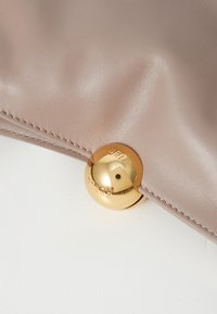 A beige leather clutch features a smooth texture, subtle sheen, and a gold circular snap closure engraved with "FURLA."