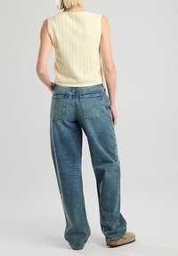 Krémový pletený svetr s vlnitým výstřihem v kombinaci se světle modrými širokými džínami s vysokým pasem; hladká textura a minimalistické zadní kapsy.