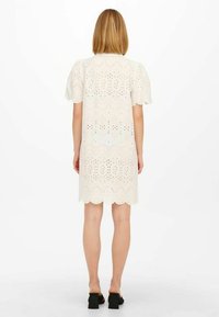 Abito bianco in broderie anglaise con orlo scallopato e maniche corte a sbuffo, caratterizzato da intricati motivi a taglio su tutto il tessuto.