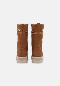 Bottines en suède brun avec un bout rond et une semelle texturée brun. Présentent un design à double bride et un petit logo doré sur le côté.