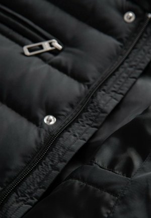 Chaqueta acolchada negra con cierre de cremallera, que presenta herrajes plateados, textura acolchada y un forro interior suave.