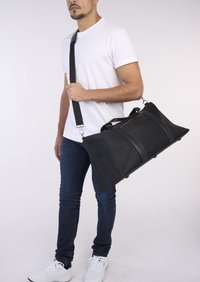 Schwarze Sporttasche mit strukturiertem Finish, Lederdetails, Doppelgriffen und verstellbarem Schultergurt, ausgestattet mit einer Reißverschlusstasche oben.