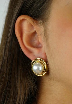 Primo piano dell'orecchio di una donna che indossa un grande orecchino rotondo di perla con una cornice in metallo dorato intrecciato.