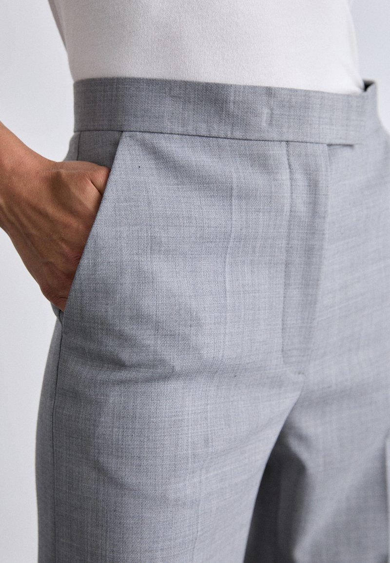 Szare spodnie o dopasowanym kroju, wykonane z lekkiego materiału. Posiadają płaski przód, boczne kieszenie oraz teksturowany wzór w tkaninie.