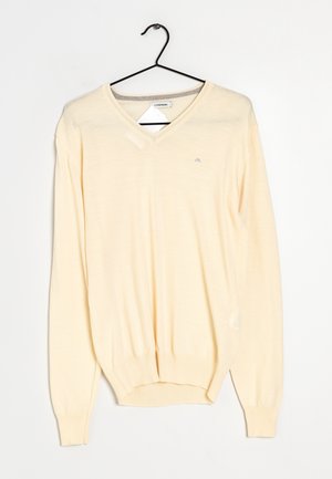 Suéter de manga larga color beige claro con cuello en V colgado en una percha de metal negra sobre un fondo blanco liso.