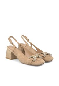 Sandalias de tacón bloque de ante beige con una correa en el tobillo y un acento decorativo de hebilla metálica en la punta. Textura suave, diseño de punta cerrada.