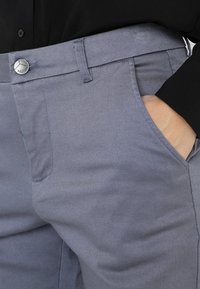 Grå bomullsblandade byxor med en slät textur, framlommor och knappstängning som har en liten logodetalj vid midjan.