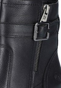 Black leather boot featuring a textured finish, side zipper, and a decorative buckle. The base has a logo embossed design.