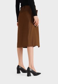 Gonna marrone a lunghezza ginocchio con un taglio sartoriale, abbinata a scarpe col tacco a bloco in pelle nera. Tessuto liscio, linee pulite e design semplice.