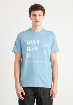 Lyseblå bomulds t-shirt med hvid tekst "CALVIN KLEIN NY" og "Calvin Klein Established 1968 NYC." Korte ærmer og rund halsudskæring.
