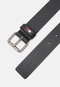 Cinturón de cuero negro con hebilla de metal plateado, que presenta una etiqueta de logo y el nombre de la marca grabado. Textura suave, diseño sencillo y múltiples agujeros.