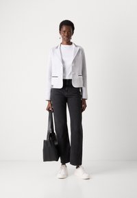 Gray knit blazer with black and white striped accents, white crew neck t-shirt, black wide-leg jeans, and white sneakers. Black bag in hand.