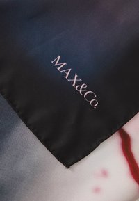 Hedvábný šátek s přechodem barev mezi černou, šedou a červenou, s tištěným abstraktním vzorem. Logo "MAX&Co." v jemně růžové barvě na spodní části.