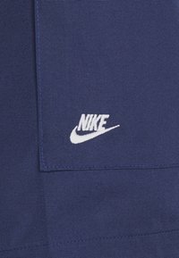 Námořnická tkanina s hladkou texturou, se bílým vyšitým logem Nike a kapsou na levé straně.