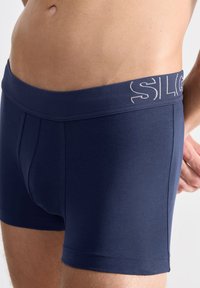 Boxer ajustados de color azul marino, confeccionados en tejido suave, con una amplia cinturilla elástica que presenta un ligero logo y un diseño ceñido.