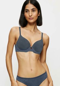 Szary stanik z wypełnieniem, ozdobiony koronką, z formowanymi miseczkami i regulowanymi ramiączkami. Posiada małą dekoracyjną kokardkę na środku.