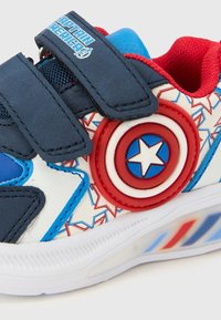 Adidași albaștri și albi cu accente roșii, având un emblemă proeminentă circulară cu scutul Captain America, materiale texturate și barete cu Velcro.