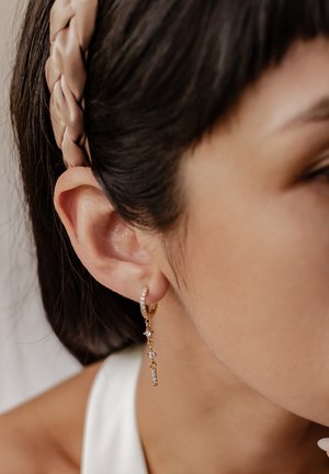 Orecchino ad arco d'oro con catena pendente di gemme chiare. Il design include una combinazione di pietre piccole e grandi per un effetto visivo interessante.