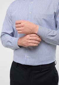 Gestreept shirt met blauw-witte verticale strepen, met knoopmanchetten, een klein borstzakje en een normale pasvorm, gecombineerd met een donkere broek.