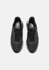 Scarpe atletiche nere con pois bianchi, dotate di tomaia in rete, colletto imbottito e suola a contrasto. I lacci e il dettaglio del logo sono visibili.