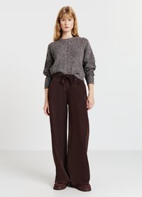 Maglione grigio a lavorazione a trecce con maniche lunghe abbinato a pantaloni marroni a vita alta e gamba larga. Il tessuto strutturato e le scarpe marroni coordinate completano il look.
