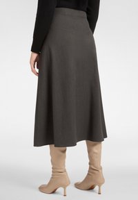 Jupe midi grise avec une texture lisse, une silhouette évasée et un éclat subtil, associée à des bottes beiges ajustées jusqu'au genou.