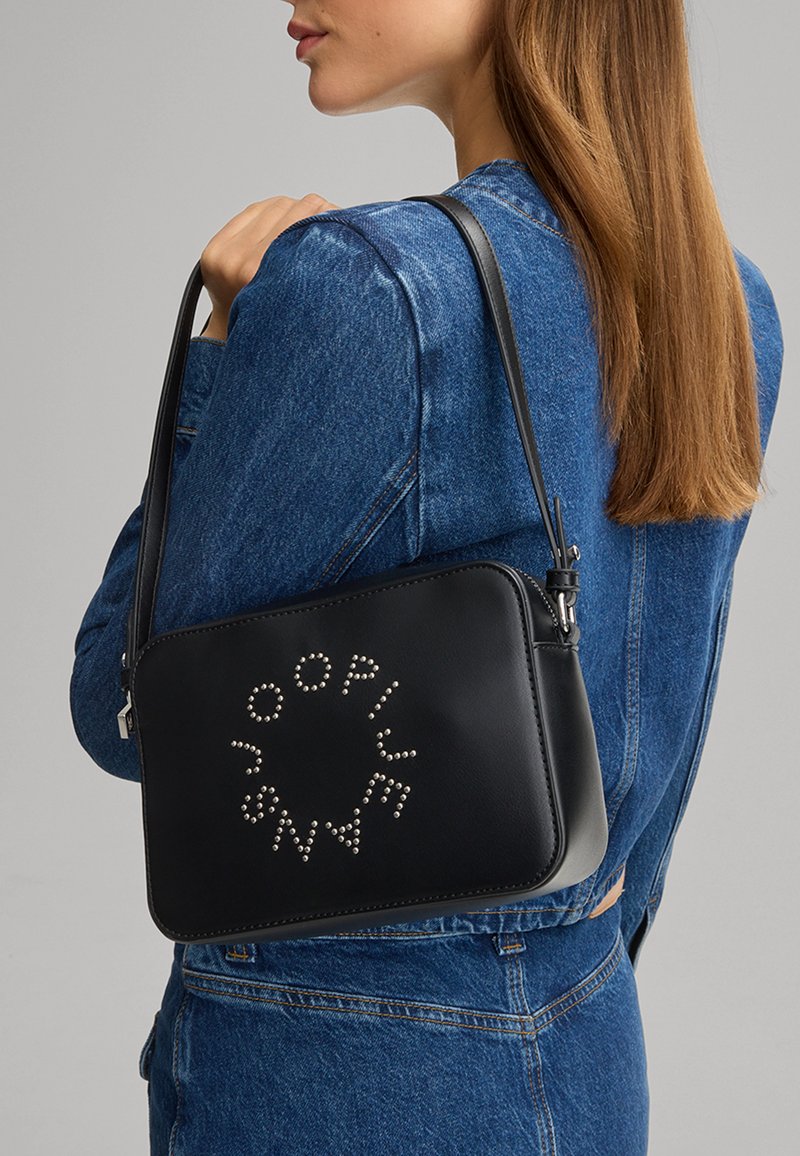 Borsa a tracolla in pelle nera con una superficie liscia, caratterizzata da borchie argentate disposte in un motivo circolare e una chiusura con zip. Include una tracolla.