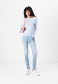 Lyseblå langermet topp med båthals, kombinert med lyseblå skinny jeans og hvite sneakers. En liten rosa crossover-veske er inkludert.