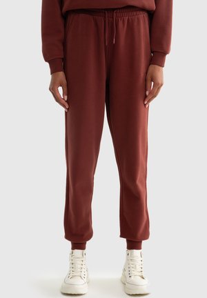 Bordeauxkleurige sweatpants met een elastische tailleband en boorden, zijzakken, gemaakt van zacht materiaal. Gepaard met witte hoge sneakers.
