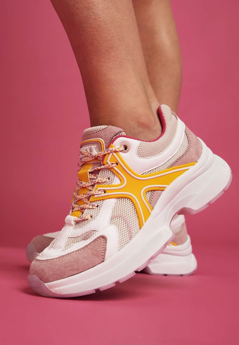 Růžové a bílé sportovní boty s síťovinovým svrškem, semišovými akcenty, žlutými detaily a texturovanými tkaničkami. Tlustá bílá podrážka s průhlednou  částí.