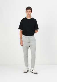Black T-shirt with white accents, paired with gray jogger pants featuring an elastic waistband and cuffed hems. White and black sneakers.