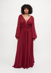 Long, deep red dress with a plunging neckline, gathered waist, and long, flowing sleeves. Made from lightweight fabric with a smooth texture.