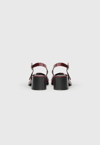 Sandali con tacco in pelle bordeaux con cinturino regolabile e tacco quadrato nero strutturato. Finitura liscia con elementi decorativi minimi.