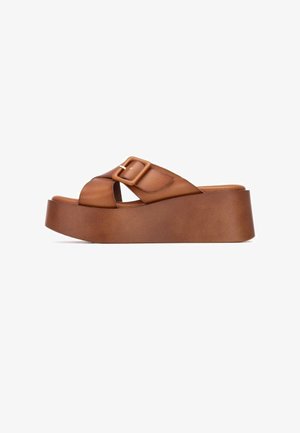 Sandalias de plataforma de cuero marrón con una correa ancha que presenta una hebilla rectangular. La suela de cuña tiene una textura suave y un diseño resistente.