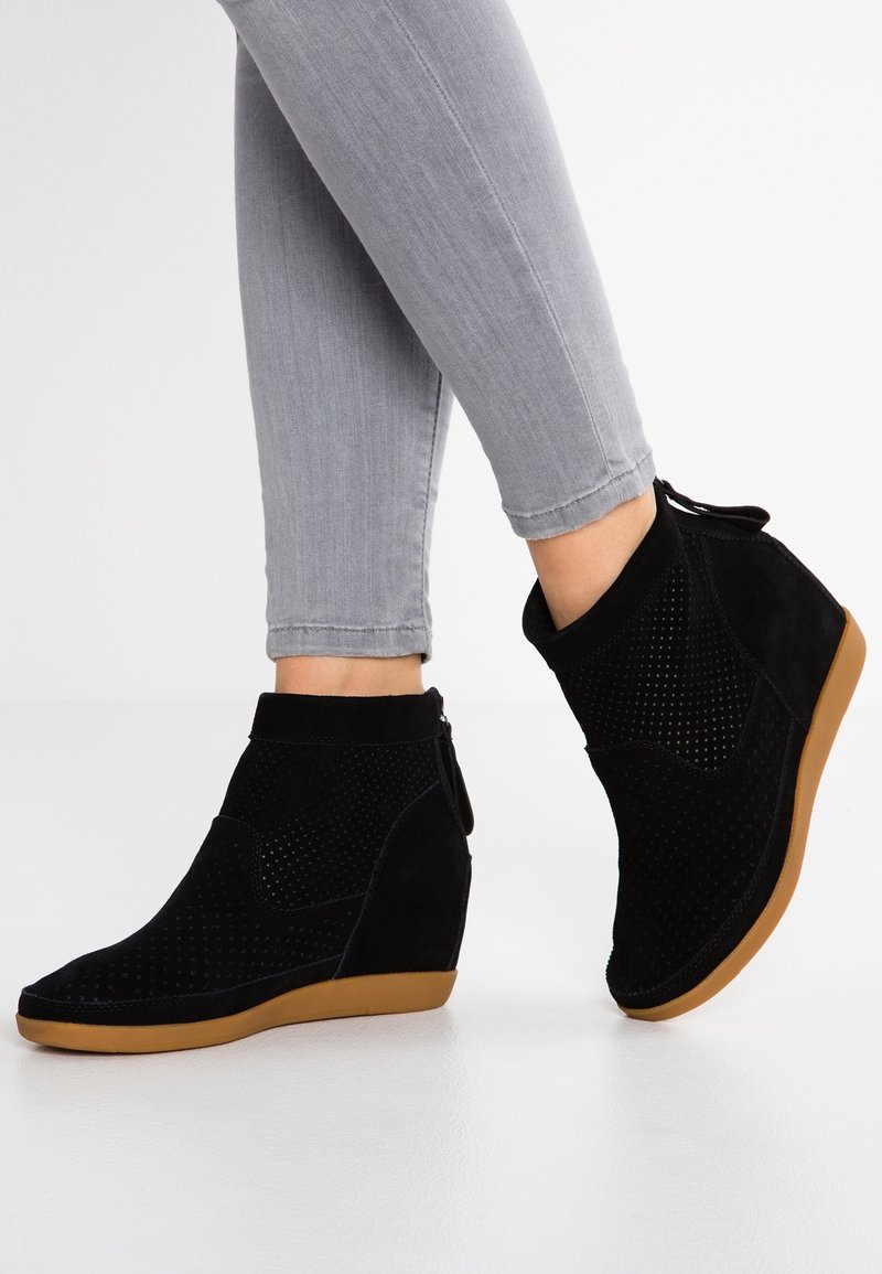 Bottines en daim noir avec talon compensé et design perforé, dotées d'une semelle en caoutchouc marron et d'une fermeture éclair latérale pour un enfilage facile.