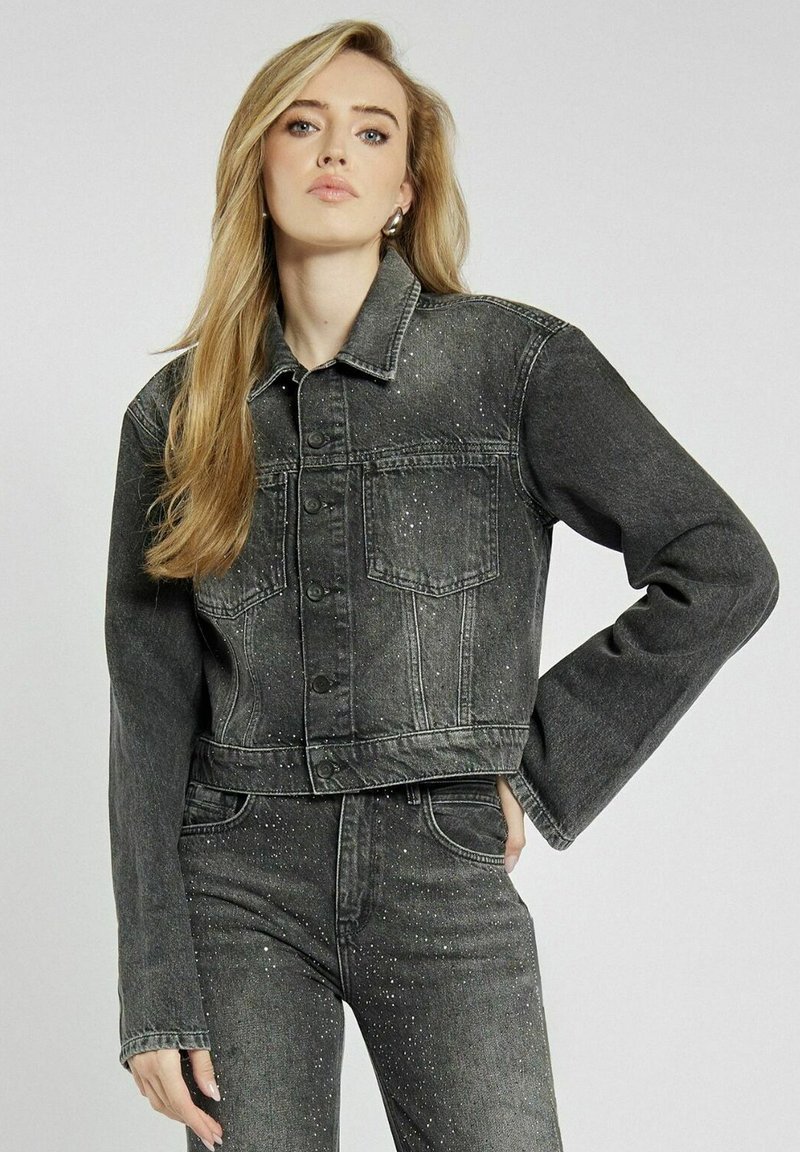 Czarna denimowa krótka kurtka z srebrnymi plamkami, z zapięciem na guziki, dwoma kieszeniami na piersi oraz szerokimi rękawami. Teksturowany materiał podkreśla design.