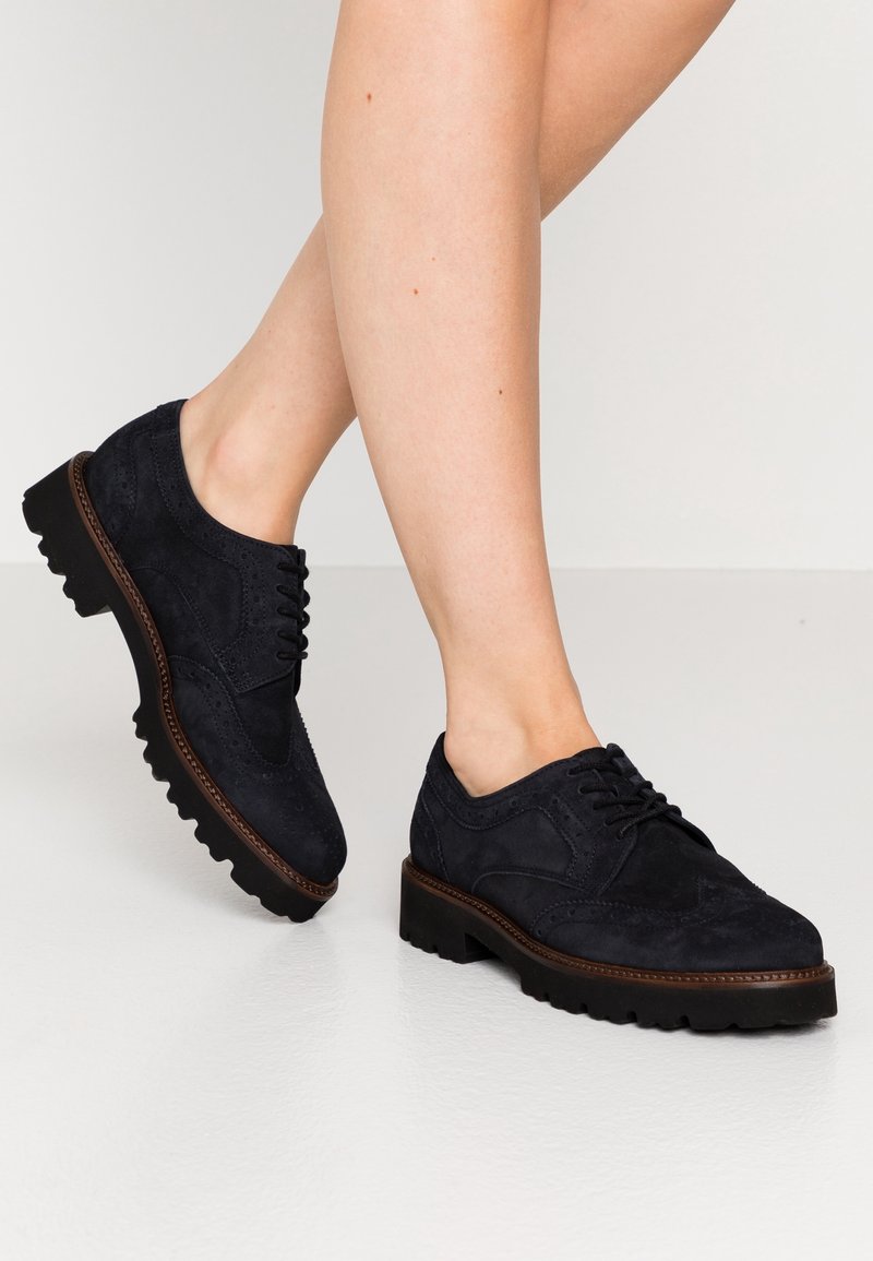 Chaussures à lacets en daim noir avec un motif brogue, dotées d'une semelle en caoutchouc épaisse et de coutures contrastantes. Style minimaliste et pratique.