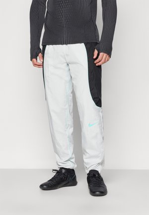 Pantalons de jogging Nike en blanc avec des panneaux latéraux noirs et des coutures en aqua, dotés d'un matériau léger et d'un design décontracté.